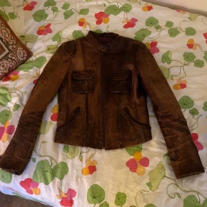 Brun skinnjacka med dragkedja - Snygg brun skinnjacka i bikerstil med coola detaljer på ärmarna. Jackan har två fickor med lock på bröstet och två snedställda fickor framtill. Stängs med dragkedja och har en stilren, lite kortare passform. Strl M men sitter mer som en S!