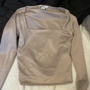 Beige långärmad topp från Amisu XS - Säljer en stilren beige långärmad topp från Amisu i storlek XS. Toppen har en fyrkantig urringning och är gjord i ett glansigt, stretchigt material som ger en lyxig känsla. Perfekt att styla med jeans eller kjol för en trendig look.