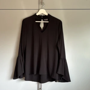 Svart blus med trumpetärmar Vero Moda - Svart blus från Vero Moda med v-ringning och snygg cut-out vid halsen. Perfekt till jeans eller kjol när du vill sticka ut lite extra❣️❣️ Strl L!!❣️❣️