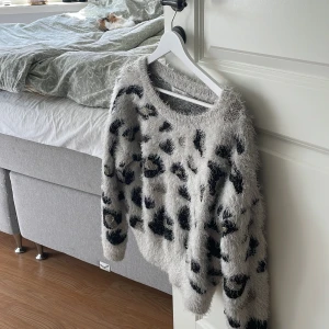 Fluffig leopardmönstrad tröja ONLY - Supermjuk och fluffig stickad tröja från ONLY med grå bas och svart leopardmönster. Tröjan har rund halsringning och långa ärmar. 