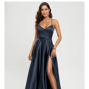 Mörkblå långklänning med slits - Elegant mörkblå långklänning i satinliknande material med smala axelband, djup v-ringning och omlottliv. Klänningen har en hög slits framtill och snygg snörning i ryggen som ger en öppen rygg-effekt. Perfekt för bal eller festliga tillfällen. Helt ny aldrig använd 