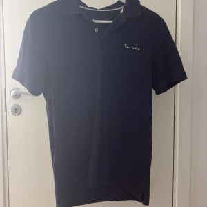 Mörkblå pikétröja från Bondelid strl S - Snygg mörkblå pikétröja från Bondelid i klassisk modell med krage och korta ärmar. Tröjan har diskret broderad logga på bröstet och är gjord i mjuk bomull som känns skön mot huden. Perfekt för en clean och stilren look. Skick 8,5/10 använd några gånger. Storleken är S men passar även XS