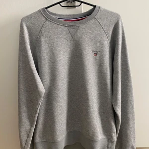 Grå sweatshirt från GANT i bomull - Klassisk grå sweatshirt från GANT med broderad logga på bröstet. Tröjan har rund halsringning, långa ärmar och är tillverkad i mjuk bomull. Perfekt för en avslappnad och stilren look.