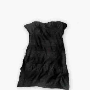 Svart glittrig kortklänning - Snygg svart kortklänning med glittriga ränder och korta ärmar. Perfekt för dig som vill sticka ut lite extra. Klänningen har en enkel, rak passform och är tillverkad i ett mjukt material som känns bekvämt mot huden.