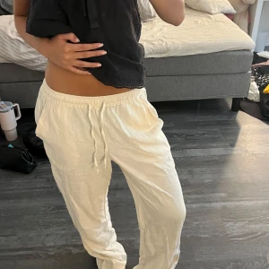 Beige linnebyxor med snörning - Säljer ett par beige linnebyxor med avslappnad passform och resår i midjan. Byxorna har snörning framtill och raka ben, perfekta för en chill och luftig stil. Materialet är linne vilket gör dem svala och sköna. MADLADY XS SHORT