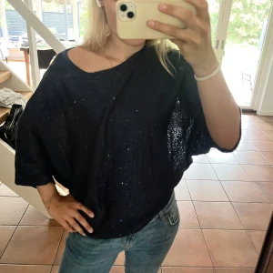 Mörkblå glittrig stickad poncho - Mörkblå stickad poncho med glittriga detaljer. Tröjan har lös passform, trekvartsärmar och bred halsringning som kan bäras lite off shoulder. Perfekt för dig som gillar en chill men ändå snygg look.