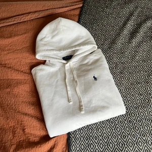 Vit hoodie från Polo Ralph Lauren - Vit hoodie från Polo Ralph Lauren i storlek xs. Tröjan har huva med snörning, känguruficka och långa ärmar. Mjuk bomullskvalitet som är perfekt för chill dagar. Enkel och stilren design som alltid funkar.