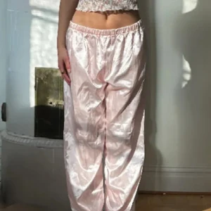 Ljusrosa satinglansiga mjukisbyxor - Säljer ett par ljusrosa mjukisbyxor med glansig satinlook och resår i midjan. Byxorna har en loose passform och raka ben, perfekta för en chill och trendig stil. Superbekväma och snygga att matcha med crop tops eller hoodies.