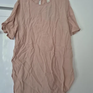 Blus - Säljer en ljusrosa blus från H&M i 100% ekologisk bomull. Blusen har rund halsringning, korta ärmar och en knappdetalj i nacken och slitsar i sidorna. Enkel och stilren modell som är perfekt för varma dagar.