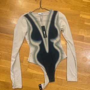 Beige och svart body från fashionnova  - Säljer en unik body från fashionnova med långa ärmar och coolt abstrakt mönster i svart och beige. Tight passform och rund halsringning. Perfekt för dig som vill sticka ut med en edgy look.