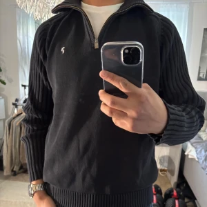 Svart stickad tröja Peak Performance XL - Svart stickad tröja från Peak Performance i storlek XL. Tröjan har ribbade ärmar, hög krage och half zip-dragkedja. Liten broderad logga på bröstet. Perfekt för kyliga dagar och snygg till jeans eller chinos.