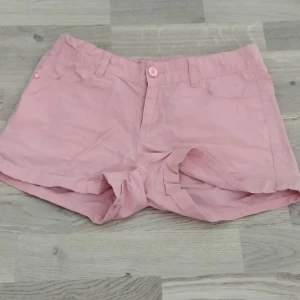 Rosa shorts från Esprit - Snygga ljusrosa shorts från Esprit med klassisk passform. De har två fickor bak, bälteshällor och stängs med knapp och dragkedja. Perfekta för varma sommadagar!