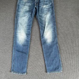 Replay jeans - Säljer ett par klassiska blå Replay jeans med snyggt slitna detaljer och raka ben. Jeansen har normal passform och är tillverkade i robust denim med tydliga ljusa partier framtill och bakfickor med dekorstickning.