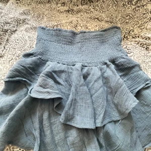 Blå volangkjol från SHEIN - Supersöt blå kjol från SHEIN med bred smock i midjan och volangdetaljer. Kjolen är kort och har en luftig känsla med snygg struktur i tyget. Perfekt för dig som gillar en chill och trendig stil.