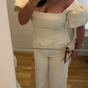 Vit puffärmad blus med fyrkantig urringning - Supersnygg vit blus med puffiga korta ärmar och fyrkantig urringning. Toppen har en figurnära passform och markerad midja med spetsig nederkant framtill. Materialet är strukturerat och ger en lyxig känsla. Perfekt för dig som vill sticka ut med en trendig och elegant look. Är normaltvis en S