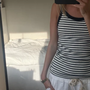 Randig ribbad linnetopp från H&M - Säljer en ribbad linnetopp från H&M i storlek M. Toppen är vit med svarta ränder och har svarta kantband, axelband och halsringning. Säljer pågrund av att det är lite stort för mig, men så himla fin till ett par linnebyxor eller jeans💕