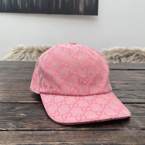 Rosa gucci keps - Snygg rosa keps från Gucci med ikoniskt GG-monogram över hela kepsen. Justerbar rem baktill i rosa läder och liten guldfärgad GG-detalj framtill. Tillverkad i bomullscanvas med exklusiv känsla, perfekt för dig som vill sticka ut med en lyxig accessoar.