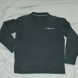 Svart Sail Racing sweatshirt - En svart sweatshirt från Sail Racing med diskret logga på bröstet och en liten logga i nacken. Tröjan har rund hals, långa ärmar och är gjord i mjuk bomullsmix. Finns nån liten fläck på tröjan men går säkert bort i tvätten.