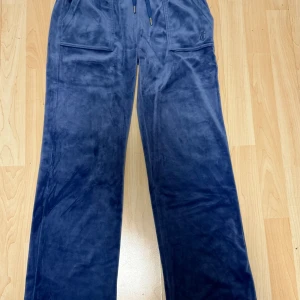 Blå velourbyxor Juicy Couture XS - Mysiga blå riktiga mjukisbyxor från Juicy Couture i velour med dragsko i midjan och stora fickor framtill. Byxorna har broderad JC-logga på ena fickan och raka ben för en chill vibe. 