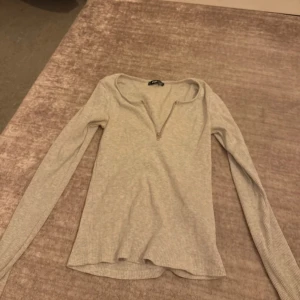 Ljusgrå ribbad långärmad tröja - Ljusgrå långärmad tröja från Fifth Avenue Shoe Repair med ribbad struktur och snygg half zip-dragkedja framtill. Tröjan har en smickrande passform och är tillverkad i mjuk bomullsmix, perfekt för lager-på-lager under hösten och våren.