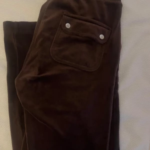 Juicy byxor xs/s - Mörkbruna manchesterbyxor med snygg snörning i midjan och stora fickor med tryckknappar bak. Byxorna har en slim passform och är perfekta för dig som gillar en mjuk och skön känsla men ändå vill se stilren ut. Byxorna är använda lite grann och är i mycket bra skick, de kommer tyvärr inte till användning längre därför säljer jag dem.