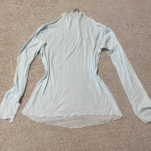 Ljusblå långärmad polotröja från Zara - Superskön och tunn ljusblå polotröja från Zara i storlek M. Tröjan är långärmad och har en lätt transparent känsla med mjukt, stretchigt material. Perfekt att styla lager på lager eller bära som den är för en clean look. Tröjan passar både för dig som han storlek S eller L!!