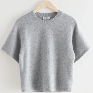 Grå stickad tröja & Other Stories - Supermjuk grå stickad tröja från & Other Stories med kort ärm och rund halsringning. Tröjan har en enkel, clean look och är gjord i ett fluffigt material som känns lyxigt. Perfekt att styla med jeans eller kjol för en chill vibe.