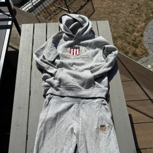 Grå hoodie från Gant med broderad logga - Säljer en grå hoodie från Gant med broderad logga och texten 'American Sportswear' på bröstet. Tröjan har huva, känguruficka och mjukt material som känns riktigt skönt. Perfekt för dig som gillar sportig och avslappnad stil. Kläd set från gant sälja båda 2 för 500kr