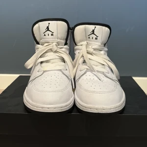 Nike Air Jordan 1 Mid vit/svart storlek 38 - Snygga Nike Air Jordan 1 Mid sneakers i vitt och svart skinn. Klassisk siluett med svart swoosh, perforerad tå och högt skaft. Tjock vit sula och svart yttersula. Ikoniska Air Jordan-loggan på sidan och Jumpman på plösen. Perfekta för dig som gillar streetstyle. orginal box finns också. pris går att diskutera vid snabb affär.