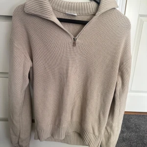 Beige stickad half zip-tröja - Beige stickad tröja med ribbad struktur och hög krage med half zip-dragkedja. Skön att ha på sig när de är kyligt eller om du ska på någon fest eller liknande 