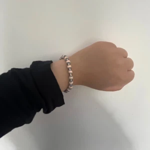 Randigt pärlarmband i silver och vitt - Snyggt armband med randiga pärlor i vitt och silver, ihopträtt på en tunn tråd och med ett smidigt silverfärgat lås. Perfekt accessoar för att ge din outfit lite extra edge. Passar dig som gillar stilrena men ändå unika detaljer. Vi har 1 av denna sort.