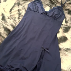 Mörkblå satin slipklänning med spets - Mörkblå kort pyjamas klänning i satin med tunna axelband, spetskant vid urringningen och nertill samt små rosetter som detalj och en slits.