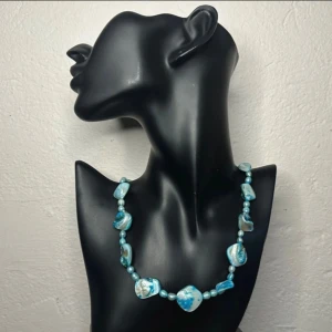 Vintage snäckhalsband i turkost och pärlemor – 60/70-tal - Elegant vintagehalsband i naturmaterial – tillverkat av skimrande snäckdelar i blått, turkost och pärlemor, varvat med pärlor som sannolikt är sötvattenspärlor eller mother-of-pearl. Halsbandet är ca 54 cm långt. 60-tal/70-tal. 