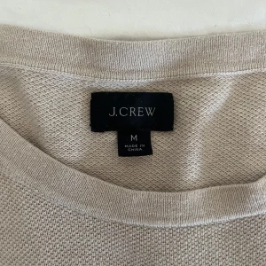 Beige stickad tröja från J.Crew - Beige stickad tröja från J.Crew i en skön mix av bomull och kashmir. Klassisk rund halsringning och långärmad modell med ribbade muddar. Perfekt för lager-på-lager och enkel att matcha med allt. Snygg basic som funkar året runt. Priset ligger runt 1200-2000kr.