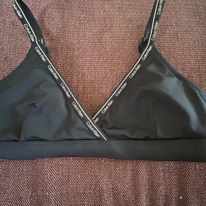 Svart bikiniöverdel Calvin Klein ! - Svart triangel  bikiniöverdel från Calvin Klein med smala axelband och vaddering (går att ta ut)  💞✌️Logotypen syns längs kanterna och axelbanden 💘 storlek 12-14 och skulle säga att den är normal i storleken 💞✌️ så fin till sommaren och passar perfekt till en vanlig svart underdel💞 