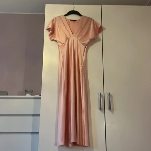 Rosa klänning från Zara - Supersnygg ljusrosa långklänning i glansigt satinmaterial. Klänningen har v-ringning, korta ärmar och ett elegant fall. Har en liten slitning av en tråd som dragits av som sträcker sig från mitten och ca 10 cm åt vänster (syns bara på nära håll) Säljes då den inte längre kommer till användning!🩷