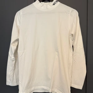 Vit polotröja med tryck på kragen - Vit långärmad polotröja från MCMXCI med svart broderad text på kragen. 