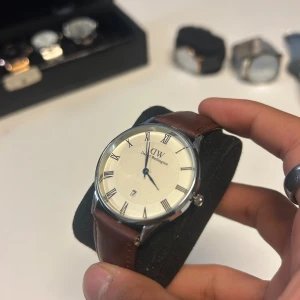 Daniel Wellington klocka brun läderrem - Stilren klocka från Daniel Wellington med klassisk vit urtavla, romerska siffror och silverfärgat hölje. Klockan har en snygg brun läderrem och minimalistisk design som passar perfekt till din outfit. Priset är inte fast 