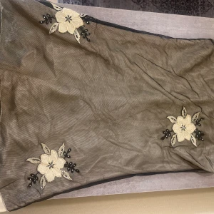 Svart meshklänning med blommor - Supersnygg kortklänning med svart mesh och broderade blommor i beige och svarta detaljer. Klänningen har ett ljust innerfoder i satin och blommorna är dekorerade med små pärlor. Perfekt för dig som vill sticka ut med en unik look.