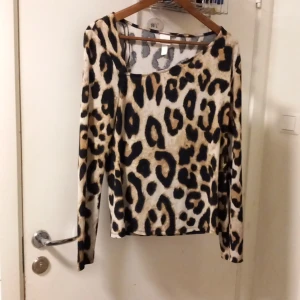 Leopardmönstrad långärmad tröja H&M - Snygg långärmad tröja från H&M med leopardmönster i beige, svart och bruna toner. Tröjan har en rak passform och rundad halsringning, perfekt för dig som vill sticka ut lite extra. Materialet är mjukt och stretchigt för en bekväm känsla.