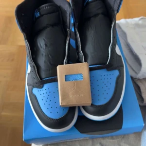 Nike Air Jordan 1 blå och svarta - Säljer ett par Nike Air Jordan 1 med blå och svarta paneler, vit sula och klassisk rund tå. Skorna har perforerad tåbox och kommer med extra blå skosnören.  Skorna är i 42,5 storlek helt nya skor använt noll gånger och är med box. Om ni är intresserade hör av dig gärna! PRISET KAN DISKUTERAS!!!!!