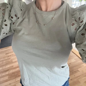 Grön topp med puffärmar och broderi - Snygg ljusgrön topp med korta puffärmar i broderad bomull och håldetaljer. Ärmarna har en romantisk känsla och toppen har en rund halsringning. Perfekt för dig som vill ha något unikt och trendigt i garderoben. Nästan aldrig använd