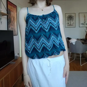 Mönstrad linnetopp i blå och turkos - Säljer en snygg linnetopp med smala axelband och ett färgstarkt zigzag-mönster i blått, turkos och svart. Toppen har en lös passform och är perfekt för varma dagar. 