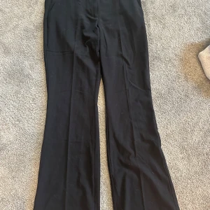 Svarta low waist kostymbyxor Nelly - Svarta kostymbyxor från Nelly i low waist-modell med utsvängda ben. Byxorna är gjorda i en mjuk mix av polyester, viskos och elastan som ger en skön passform. Perfekta för en clean och trendig look. Använda max tre gånger så som nya i skicket. 