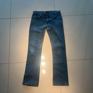 Blå bootcut/strait lowrise jeans - Snygga blå jeans från Tiger of Sweden med klassisk femficksdesign och bootcut/strait Ben. Jeansen är ochså lowrise med svarta knappar, har ochså en lätt design på bakfickorna.