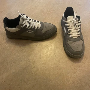Grå sneakers från Hugo med vit detalj - Ganska nya och nästan helt oanvända hugo sneakers i storlek 42. Tyvärr utan något kvitto eller skopaket