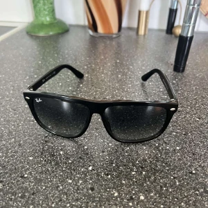 Svarta Ray-Ban Wayfarer solglasögon - Klassiska svarta Ray-Ban Wayfarer solglasögon med bred plastbåge och mörka glas. Snygg och tidlös modell med Ray-Ban-logga på skalmen. Tillverkade i Italien och perfekta för att lyfta din stil.