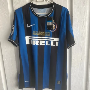 Inter Milan Sneijder 10 Finaltröja Nike - Inter Milan fotbollströja med Sneijder 10 på ryggen, Champions League-final 2010-tryck och Pirelli sponsor. Klassisk blå och svart randig design, Nike-logga och klubbmärke på bröstet. Kortärmad och tillverkad i lätt, ventilerande material.