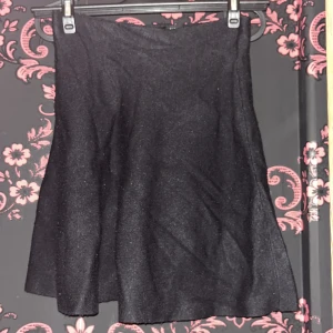 Svart glittrig kortkjol från ONLY - Supersnygg svart glittrig kortkjol från ONLY. Kjolen har en lätt utsvängd form och är perfekt om du vill sticka ut lite extra. Materialet är mjukt och skimrar snyggt i ljuset. Enkel att matcha med både sneakers och boots.