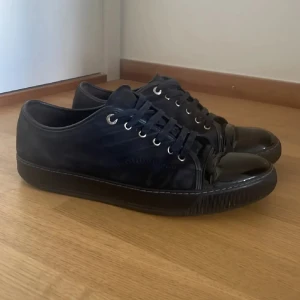 Lanvin skor - Snygga svarta sneakers från Lanvin med mattsvart mocka och glansig lackad tå. Skorna har snörning med metallöljetter och en platt sula. Perfekta för dig som gillar stilrena och exklusiva detaljer.